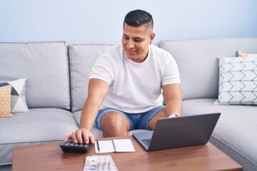 Young latin man using laptop accounting at home