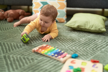 Adorable toddler lying on floor playing with car toy at home