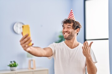 Hispanic young man wearing birthday hat doing video call with smartphone celebrating achievement with happy smile and winner expression with raised hand
