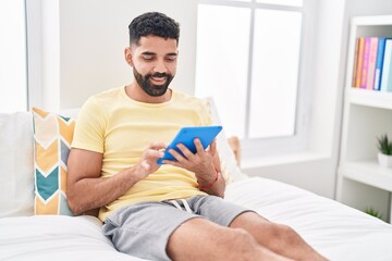 Young arab man using touchpad sitting on bed at bedroom
