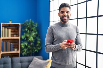 Young hispanic man smiling confident using smartphone at home