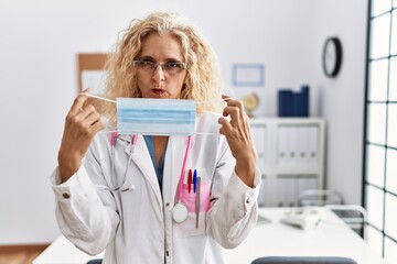 Middle age blonde woman wearing doctor uniform and medical mask skeptic and nervous, frowning upset because of problem. negative person.