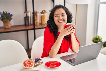 Young chinese woman having breakfast using laptop at home