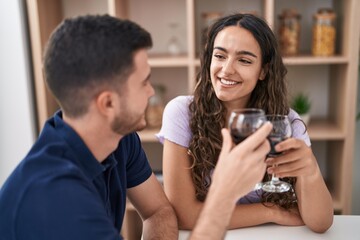 Young hispanic couple drinking wine sitting on table at home