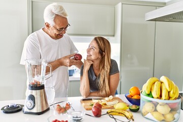 Middle age hispanic couple smiling happy cooking smoothie at the kitchen.