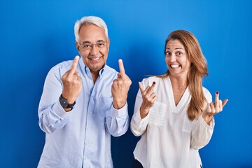 Middle age hispanic couple standing over blue background showing middle finger doing fuck you bad...