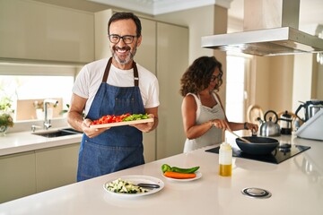 Middle age couple cooking mediterranean food at home winking looking at the camera with sexy...
