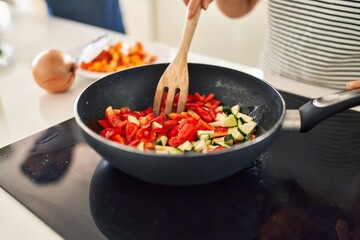 Middle age hispanic couple cooking food on frying pan at kitchen