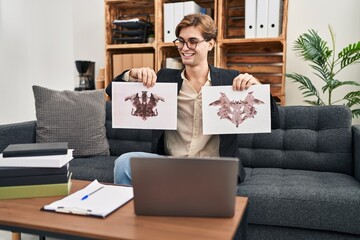 Young therapist man working with rorschach test at psychology clinic winking looking at the camera...