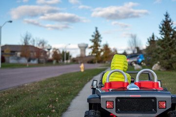 Caucasian boy driving an electric toy car down a sidewalk.