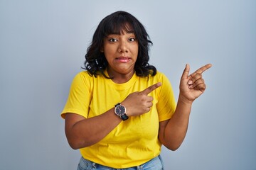 Hispanic woman standing over blue background pointing aside worried and nervous with both hands,...
