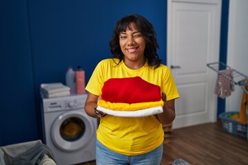 Hispanic woman holding clean laundry winking looking at the camera with sexy expression, cheerful...