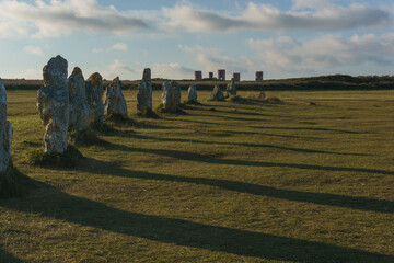 Alignment of menhir stones during golden hour with shadows on green meadow, Camaret-sur-Mer,...