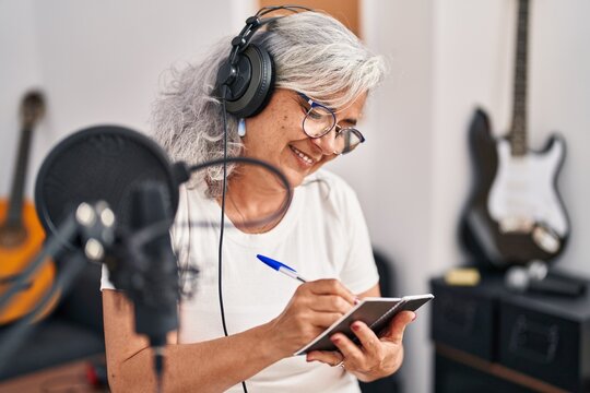 Middle age woman musician writing on notebook at music studio