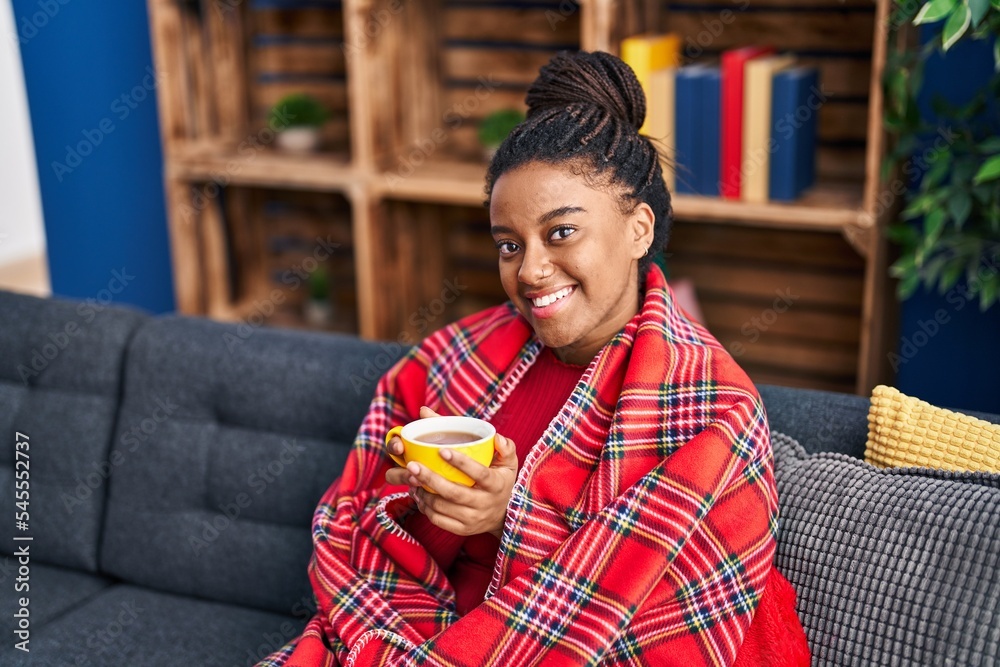 Wall mural African american woman drinking coffee sitting on sofa at home