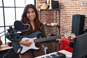 Obraz na płótnie Canvas Young hispanic woman artist playing electrical guitar at music studio