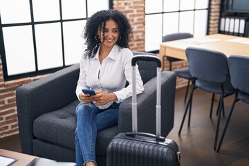 Young hispanic woman business worker using smartphone waiting for travel at office