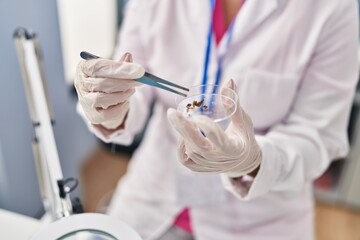 Young beautiful hispanic woman scientist holding plant sample and tweezers at pharmacy