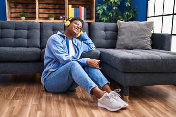 African american woman listening to music sitting on floor at home