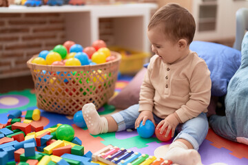 Adorable toddler playing with balls sitting on floor at kindergarten