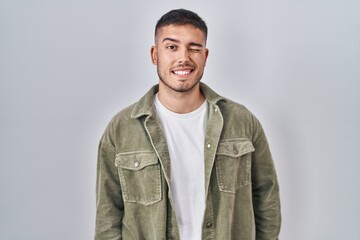 Young hispanic man standing over isolated background winking looking at the camera with sexy expression, cheerful and happy face.