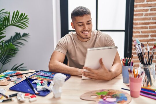 Young hispanic man artist smiling confident drawing on notebook at art studio