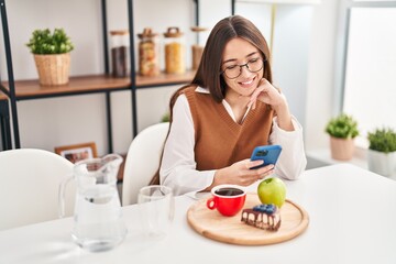 Obraz na płótnie Canvas Young beautiful hispanic woman having breakfast using smartphone at home