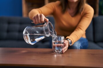 Middle age woman pouring water sitting on sofa at home