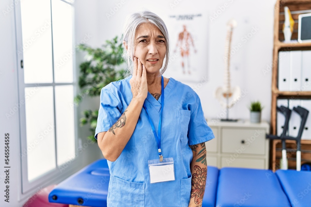 Sticker middle age grey-haired woman wearing physiotherapist uniform at medical clinic touching mouth with h