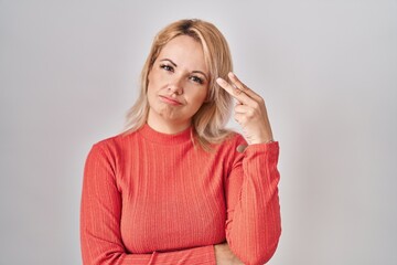 Blonde woman standing over isolated background shooting and killing oneself pointing hand and fingers to head like gun, suicide gesture.