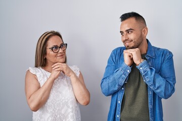 Hispanic mother and son standing together laughing nervous and excited with hands on chin looking...