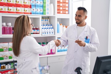 Fototapeta na wymiar Man and woman pharmacist smiling confident shake hands at pharmacy