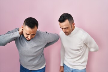 Homosexual couple standing over pink background suffering of backache, touching back with hand, muscular pain