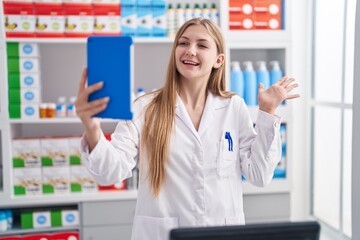 Young caucasian woman working at pharmacy drugstore doing video call with tablet celebrating achievement with happy smile and winner expression with raised hand