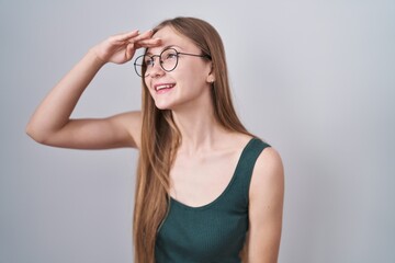 Young caucasian woman standing over white background very happy and smiling looking far away with hand over head. searching concept.