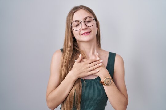 Young caucasian woman standing over white background smiling with hands on chest with closed eyes and grateful gesture on face. health concept.