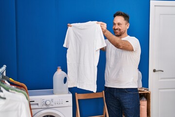 Young caucasian man smiling confident holding clean t shirt at laundry room - Powered by Adobe