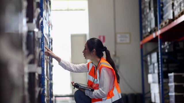 Professional beautiful asian woman worker checks stock and inventory with holding clipboard in the retail warehouse full of shelves with goods. Working in logistics, Distribution center.