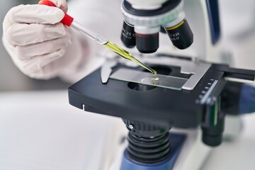 Young hispanic man scientist using microscope working at laboratory