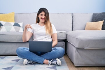 Obraz premium Young brunette woman sitting on the floor at home using laptop smiling happy pointing with hand and finger