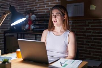Brunette woman working at the office at night winking looking at the camera with sexy expression,...