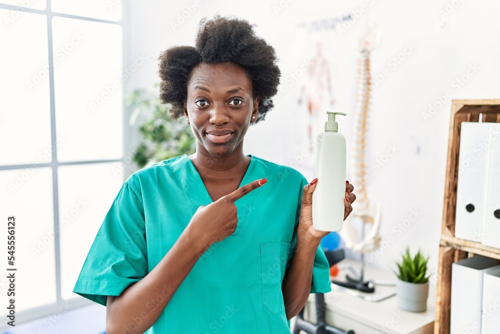 Sticker African young physiotherapist woman holding massage body lotion smiling happy pointing with hand and finger