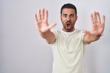 Hispanic man with beard standing over isolated background doing stop gesture with hands palms, angry and frustration expression