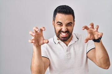 Young hispanic man with beard wearing casual clothes over white background smiling funny doing claw...