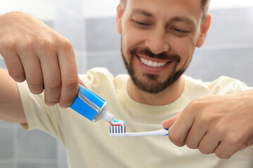 Man applying toothpaste onto brush in bathroom, focus on hands