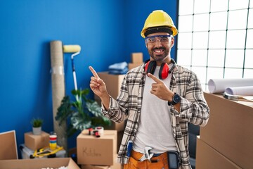 Young hispanic man with beard working at home renovation smiling and looking at the camera pointing with two hands and fingers to the side.