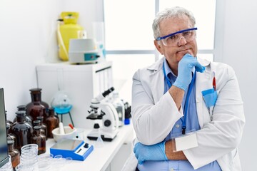 Middle age grey-haired man wearing scientist uniform with arms crossed gesture at laboratory