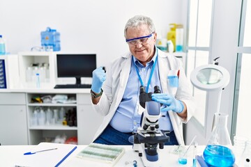 Senior caucasian man working at scientist laboratory very happy and excited doing winner gesture with arms raised, smiling and screaming for success. celebration concept.