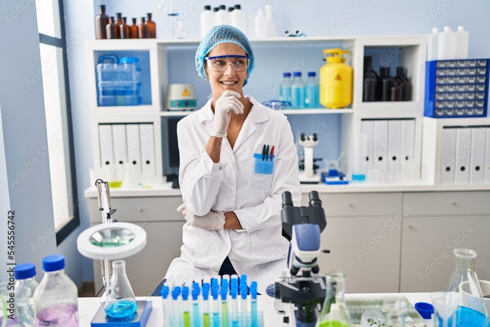 Poster brunette woman working at scientist laboratory with hand on chin thinking about question, pensive ex