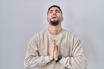 Young handsome man standing over isolated background begging and praying with hands together with...